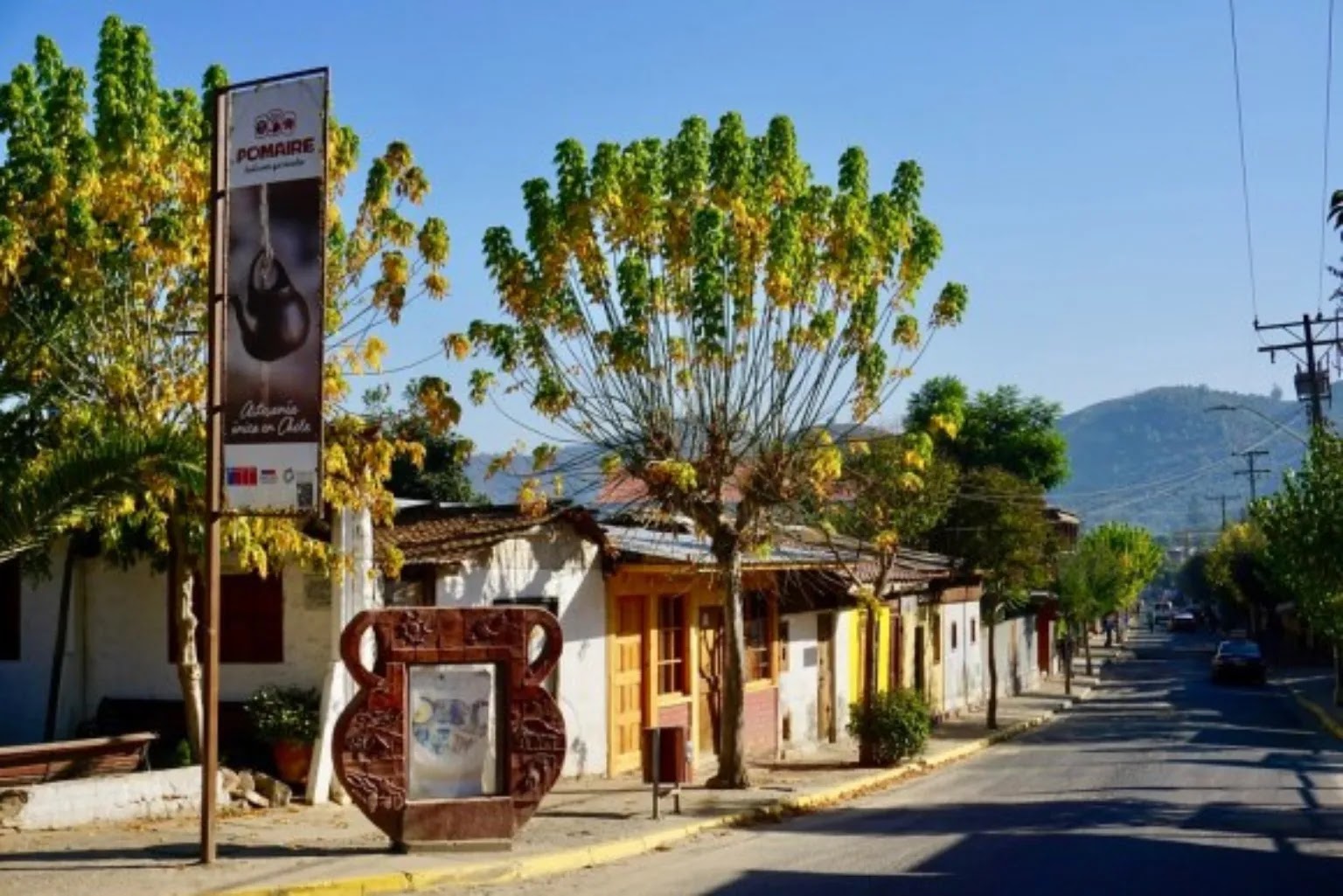 Calle típica de Pomaire con letrero de artesanía y árboles